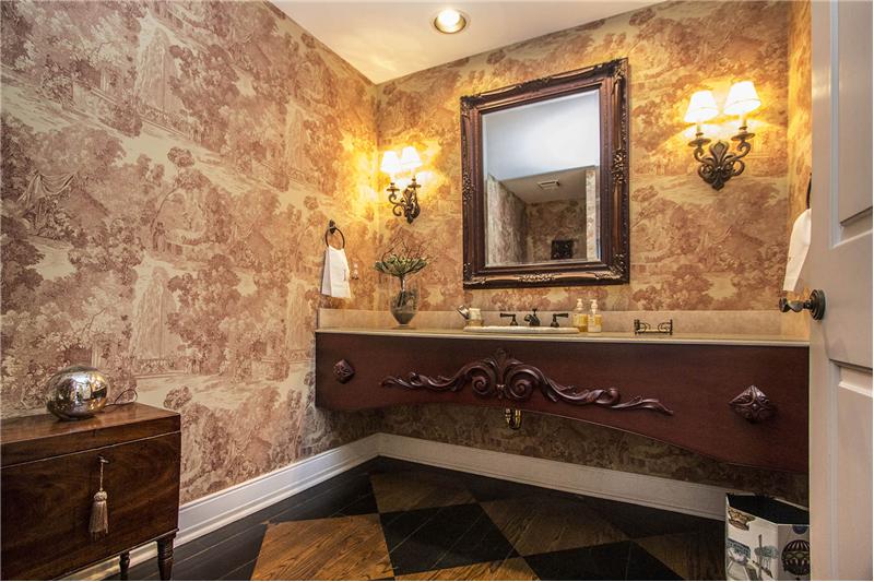 Located off the Foyer, the Powder Room features custom hardwood flooring, an ornate custom vanity, and sconce lighting